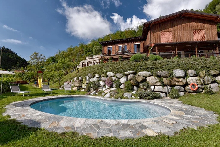 Holzbauernhaus mit Pool, umgeben von Grün, zwischen Hügeln und Natur